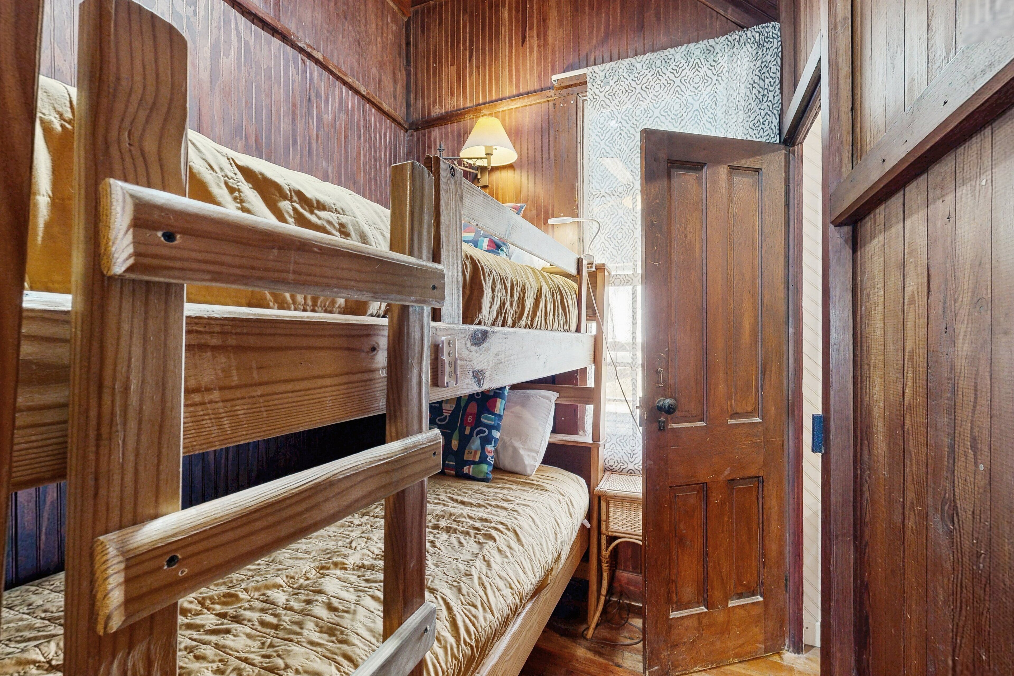 A wooden bunk bed room with a small desk and a door.