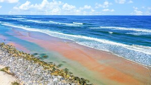 Een strand met helderblauw water, een rotsachtige kustlijn en een heldere lucht.