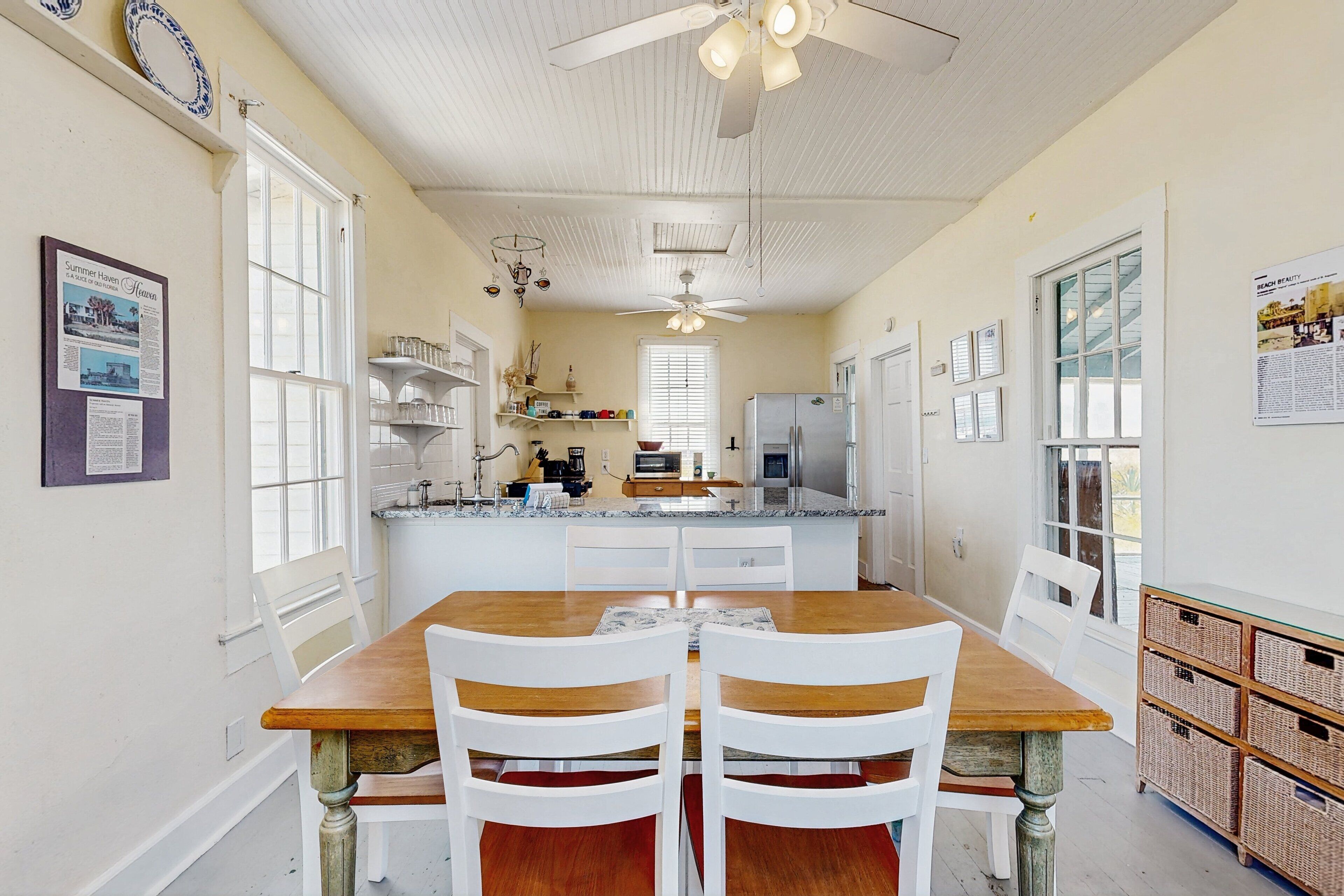 A kitchen with a wooden table and white chairs, a ceiling fan, and a refrigerator.