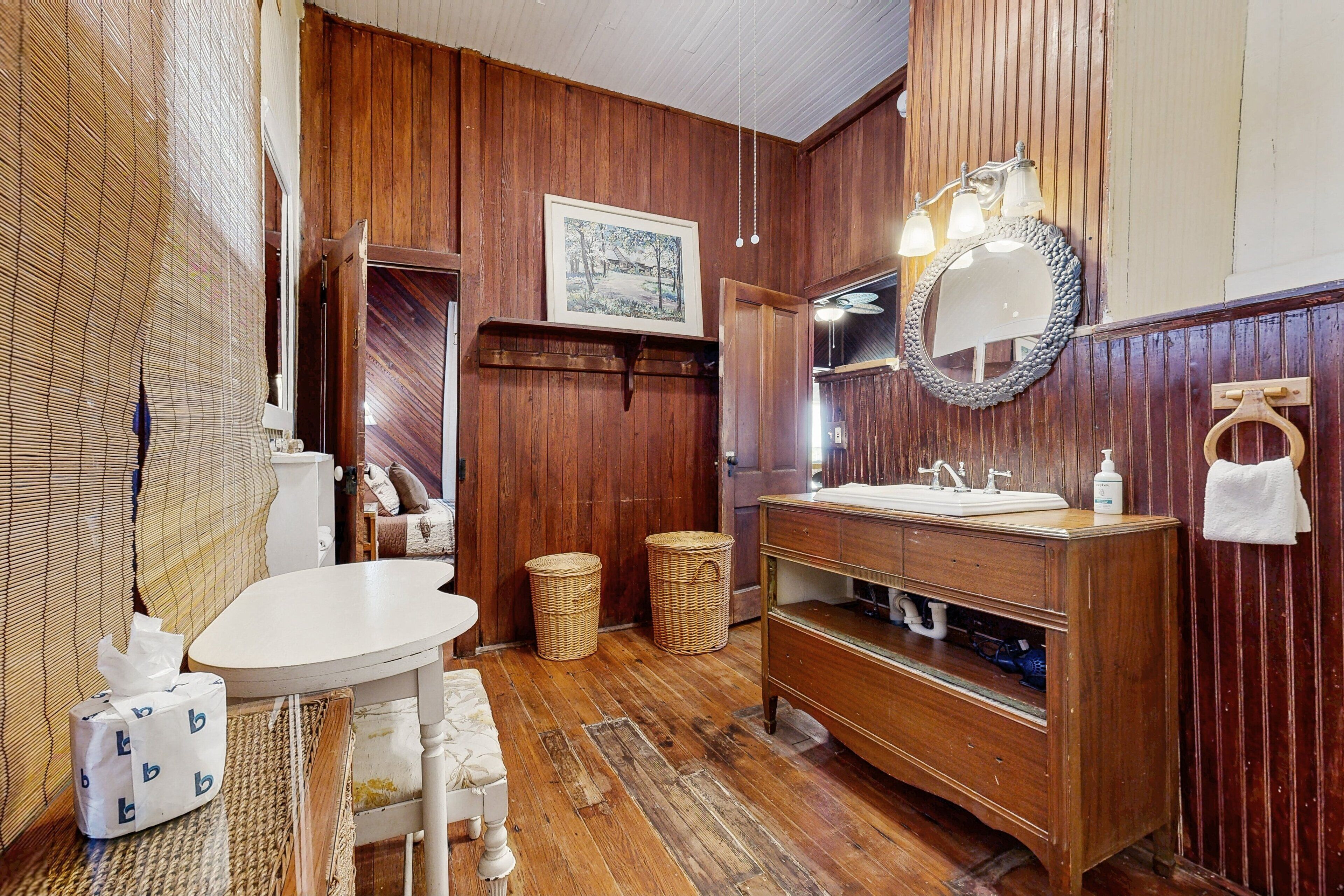 A wooden-paneled bathroom with a wooden vanity, a round mirror, and a small table with a chair.