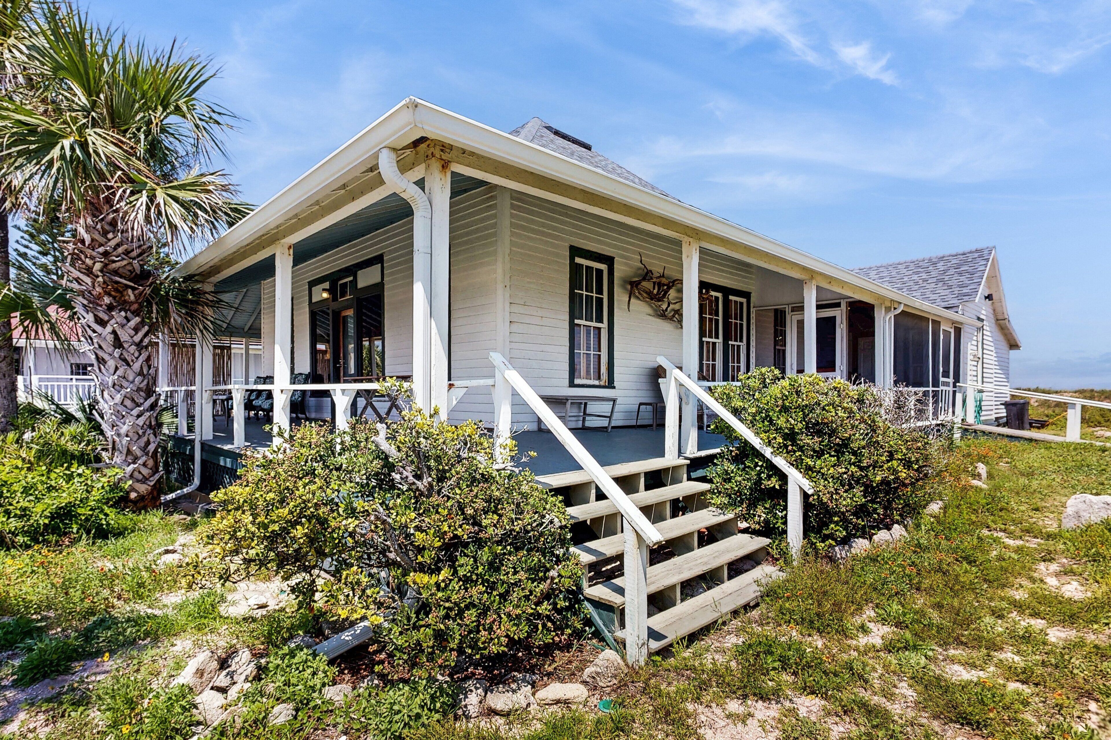 A white colonial-style house with a porch, steps, and a palm tree in the foreground.