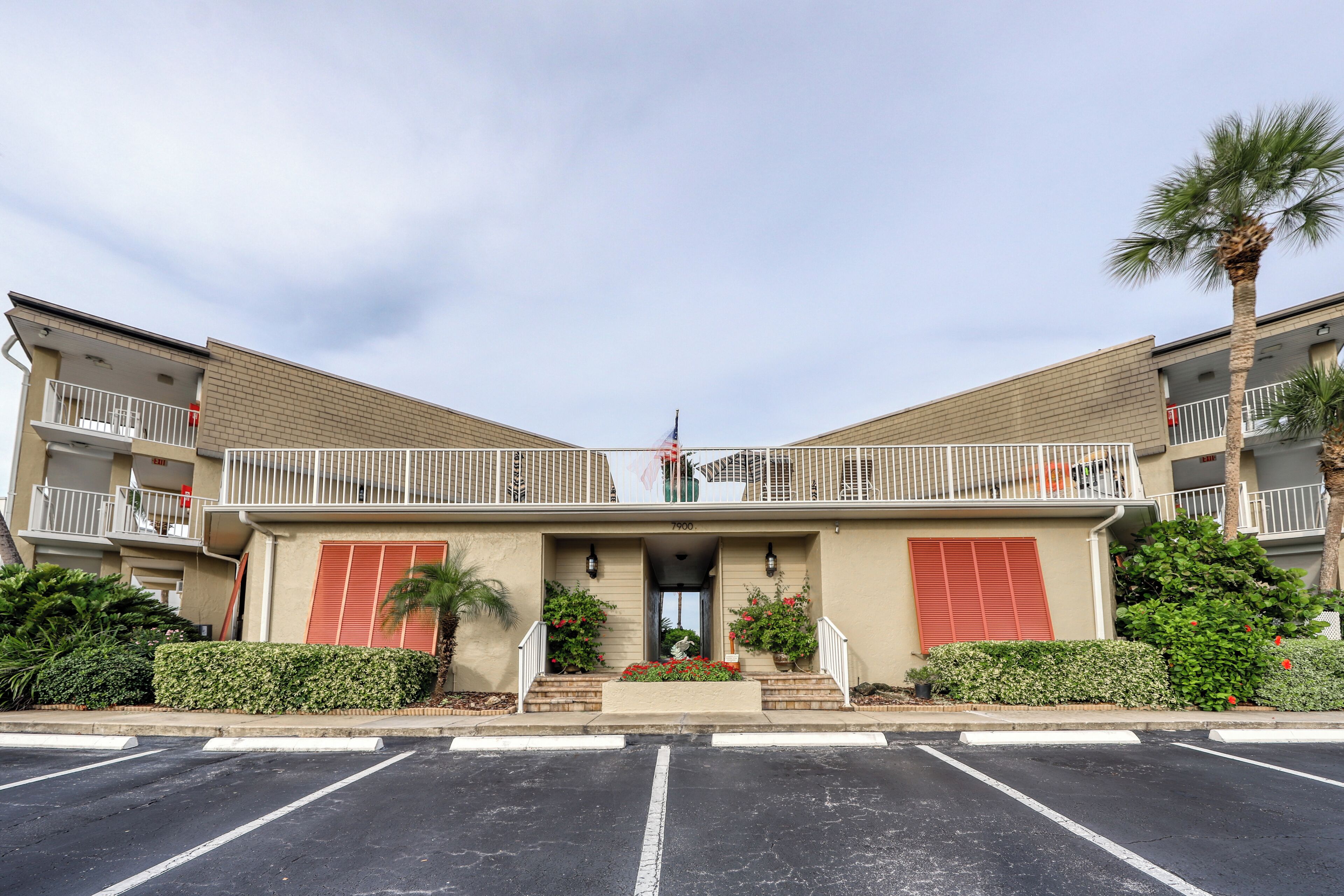 A two-story building with a central entrance, a small balcony, and a parking lot in front.