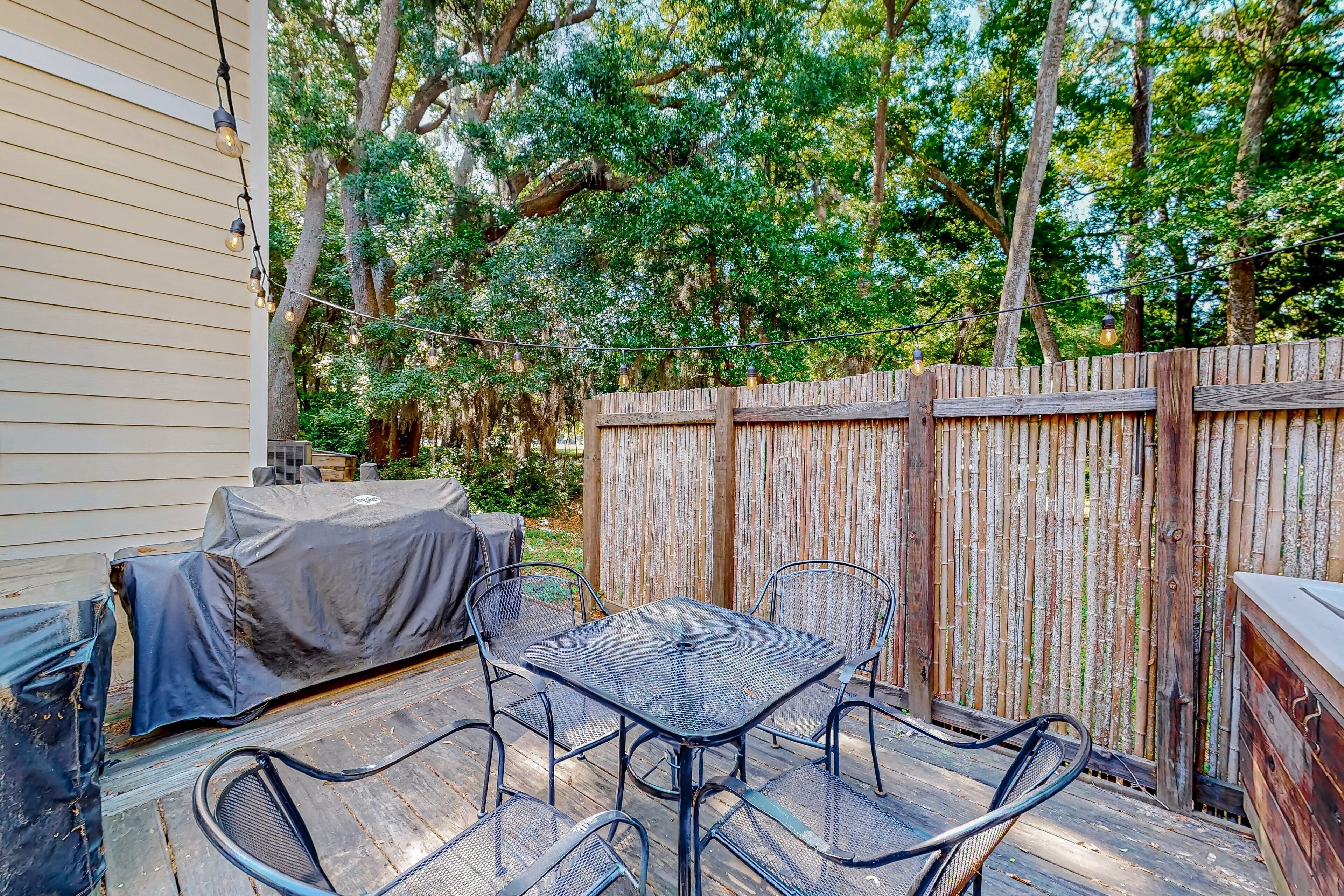 A covered patio with a table and chairs, a barbecue grill, and a wooden fence.