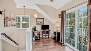 A spacious living area with a wooden floor, a ceiling fan, a TV, and a large window with curtains. - Inviting Waterfront Cottage w Separate Garage Apartment and Stunning Marsh View (Fernandina Beach)