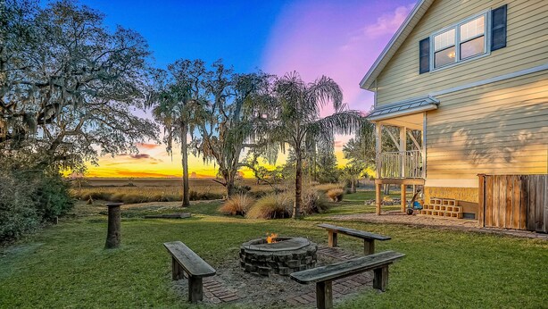 A backyard with a fire pit, picnic tables, and a house with a porch. - Inviting Waterfront Cottage w Separate Garage Apartment and Stunning Marsh View (Fernandina Beach)