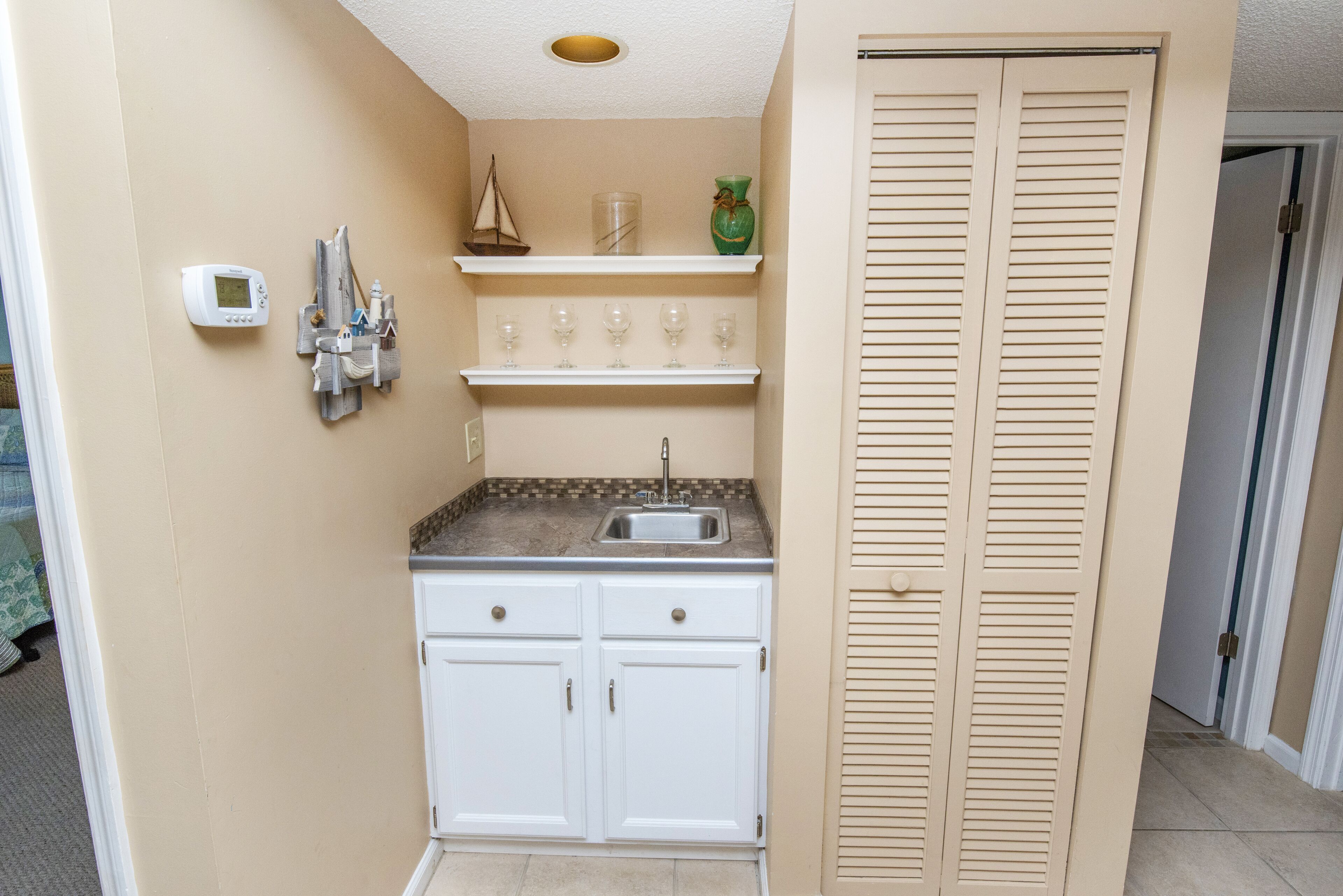 A compact kitchen with white cabinets, a built-in sink, and a small shelf with decorative items.