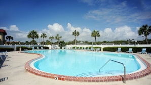 Una piscina con borde de azulejos, rodeada de tumbonas y palmeras.