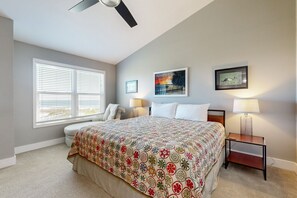 Une chambre à coucher comprenant un lit, une table de chevet, un ventilateur de plafond, une fenêtre avec des stores et deux lampes fixées au mur.