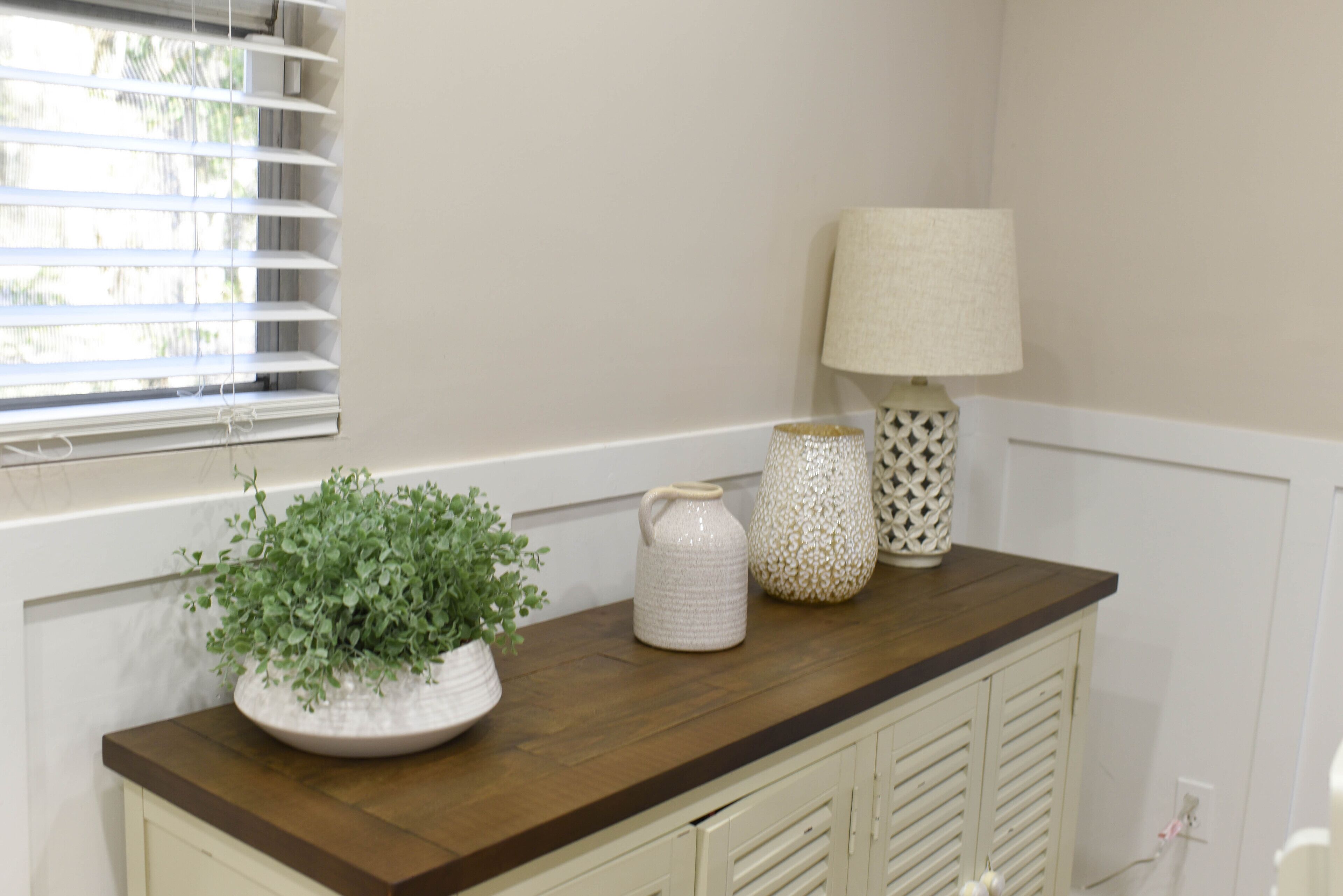 A kitchen counter with a potted plant, a white pitcher, and a patterned lamp.