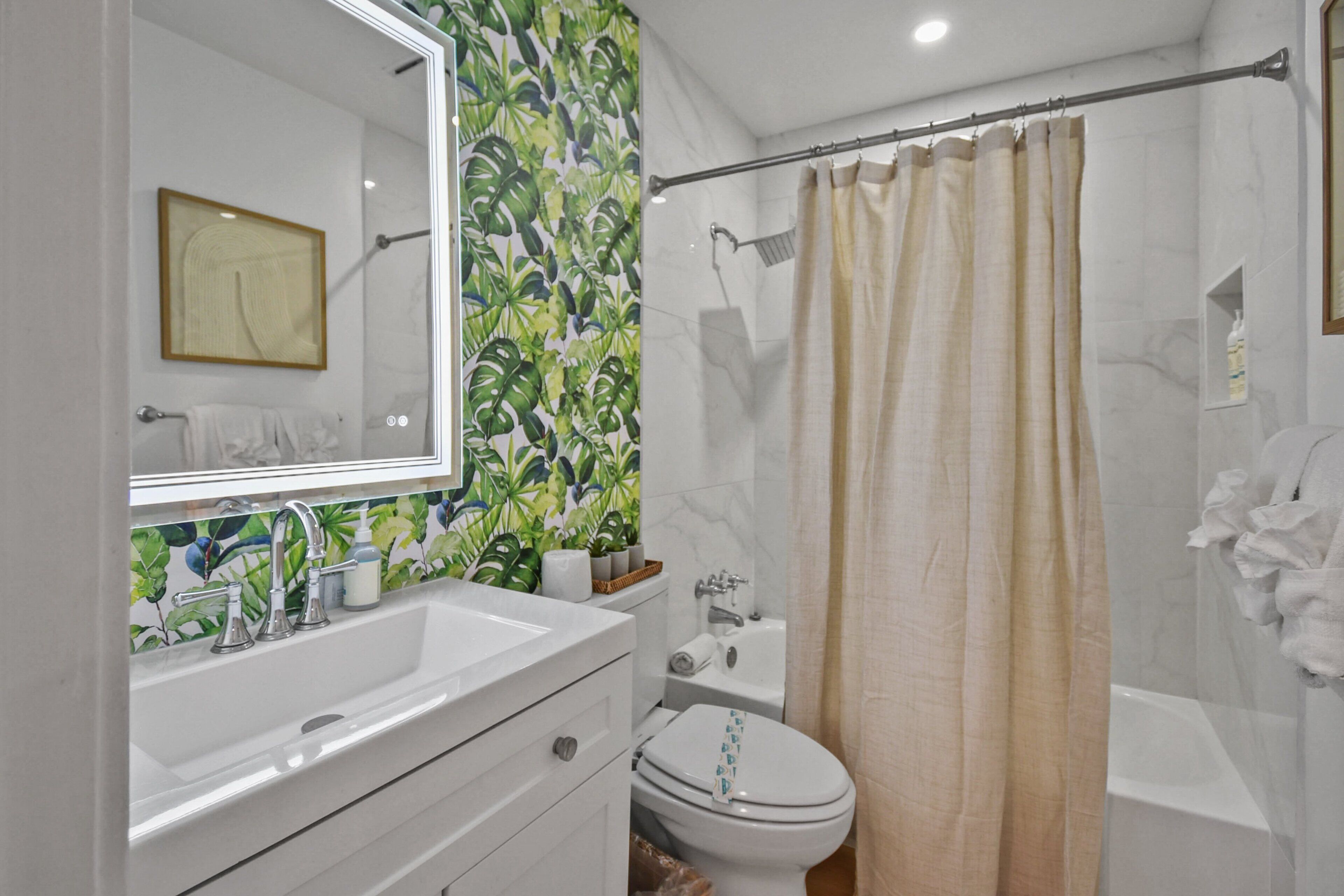 Un baño con lavamanos blanco, espejo, inodoro y bañera.