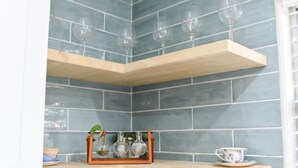 A corner with two wooden shelves against a tiled wall, holding glassware and a floral cup. - Family & Pet-friendly Home Near Beach, Downtown & Boat Ramp (St. Augustine)