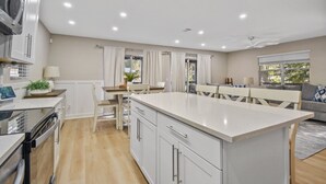 A modern kitchen with white cabinetry, a central island, and a dining area with a table and chairs. - Family & Pet-friendly Home Near Beach, Downtown & Boat Ramp (St. Augustine)