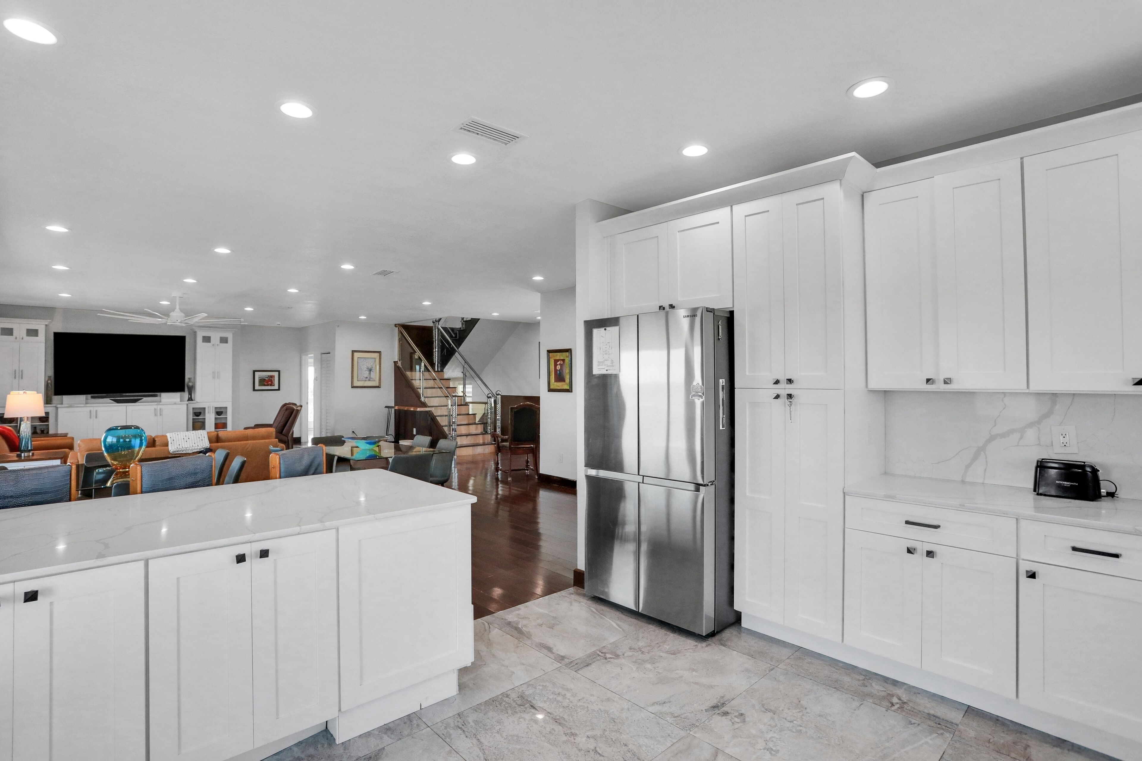 A modern kitchen with white cabinets, a stainless steel refrigerator, and a marble countertop.