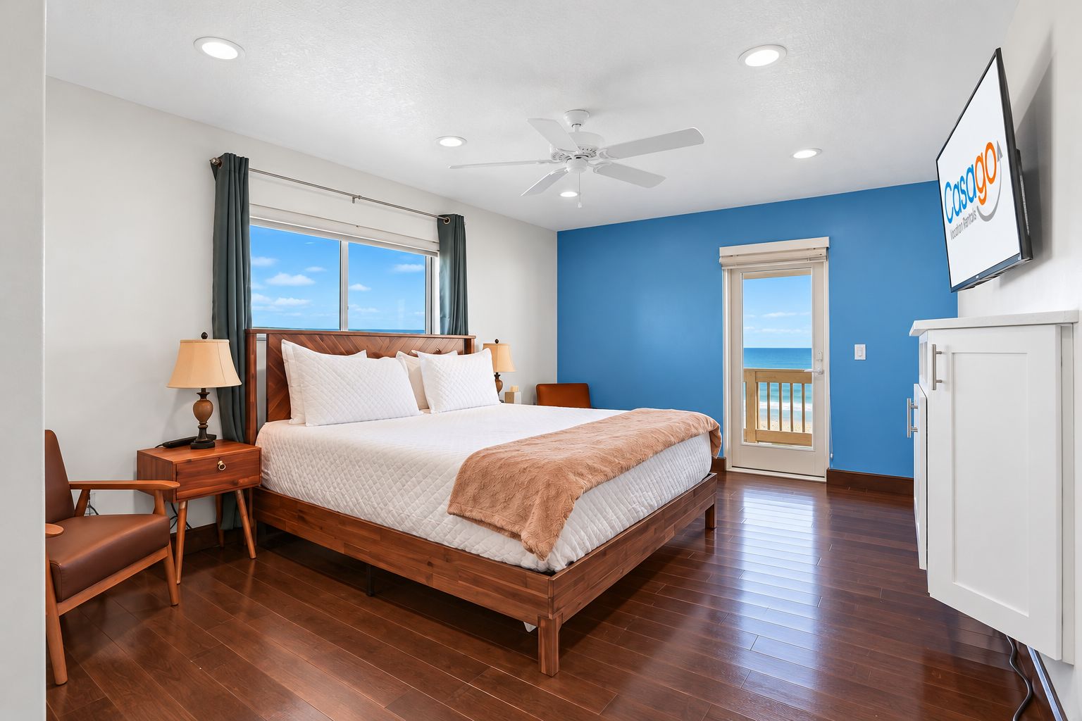 A hotel room with a bed, a desk, a chair, a TV, and a view of the ocean.