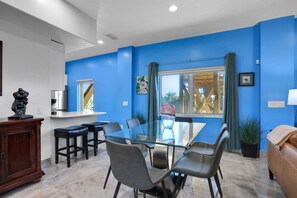 A modern dining area with a glass table and chairs, a wooden cabinet, and a blue accent wall. - Immaculate, Modern Stay Steps to Beach With Amazing Ocean Views (Flagler Beach)