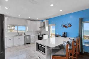 A modern kitchen with white cabinets, a central island, and a view of the ocean. - Immaculate, Modern Stay Steps to Beach With Amazing Ocean Views (Flagler Beach)