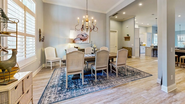 A spacious dining area with a chandelier, white chairs, and a blue patterned rug. - Golf Course-view Home Near Beaches With Deck, Porch, Grill, Streaming, W/d, & AC (St. Simons Island)