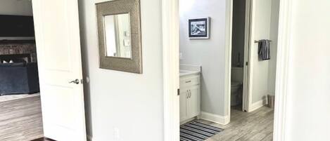 A hallway with a door, a framed picture, a radiator, and a bathroom visible in the background.