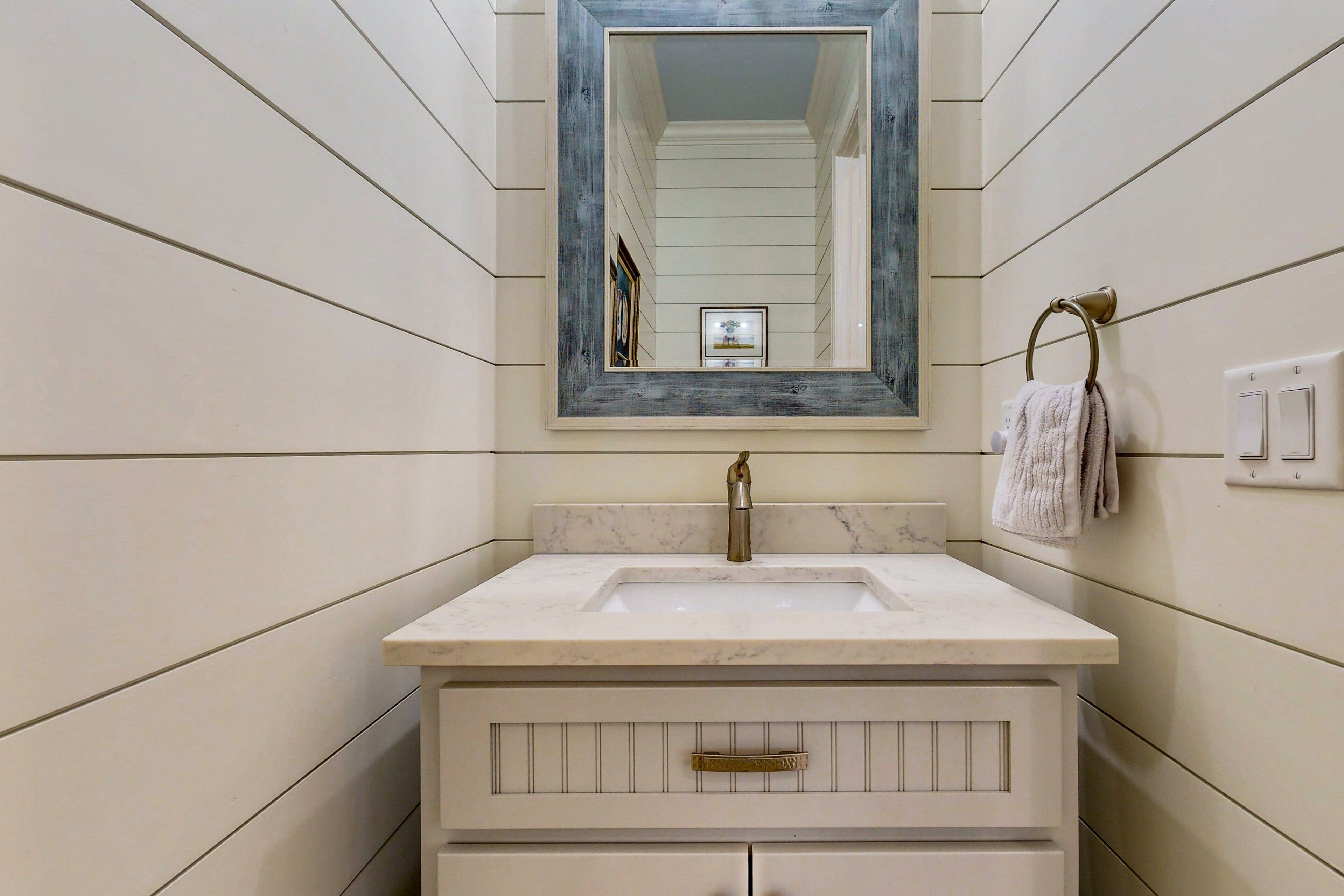 A bathroom with a white vanity, a mirror with a wooden frame, and a towel rack.