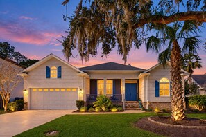 A two-story house with a garage, a front porch, and a well-maintained lawn. - Golf Course-view Home Near Beaches With Deck, Porch, Grill, Streaming, W/d, & AC (St. Simons Island)