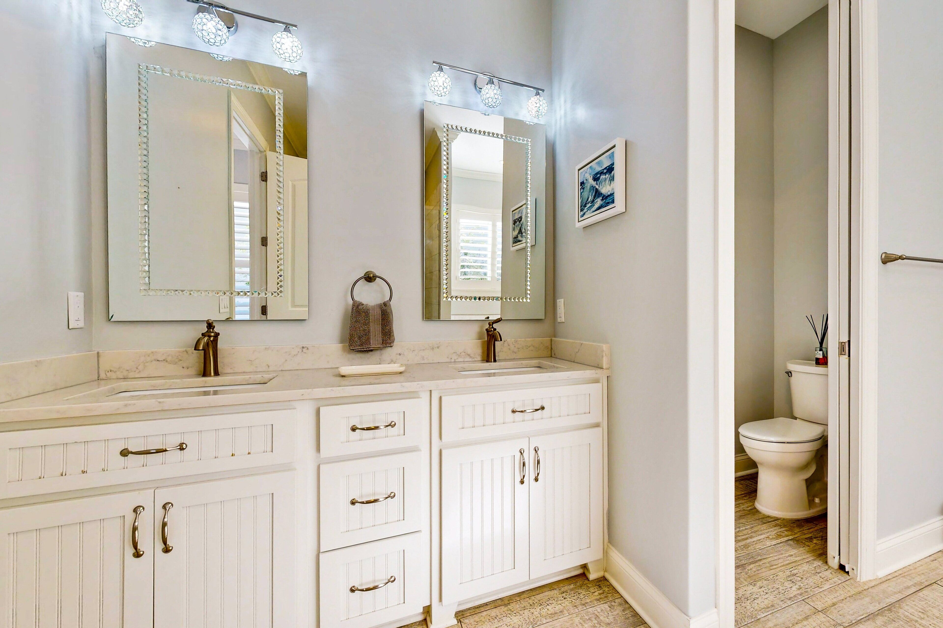 A bathroom with a double vanity, two mirrors with lights, a sink, and a toilet.