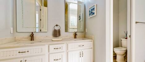 A bathroom with a double vanity, two mirrors with lights, a sink, and a toilet.