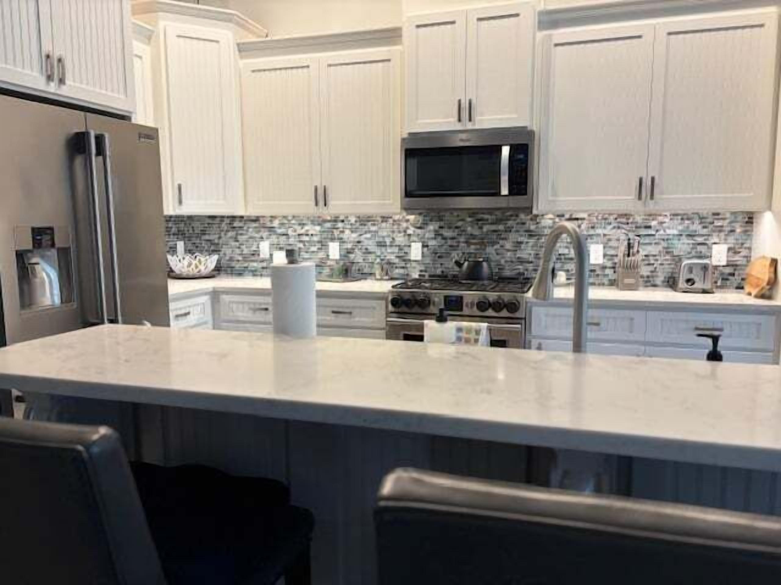 A modern kitchen with white cabinets, a stainless steel refrigerator, a microwave, a stove, and a marble island.