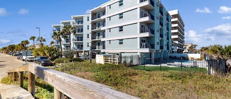 A multi-story residential building with balconies, a wooden boardwalk, and a fenced pool area.