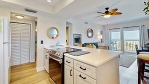 A modern kitchen with white cabinetry, a central island, and a ceiling fan. - Modern Oceanfront Condo With Outdoor Pool, Balcony, & Washer/dryer (Jacksonville Beach)