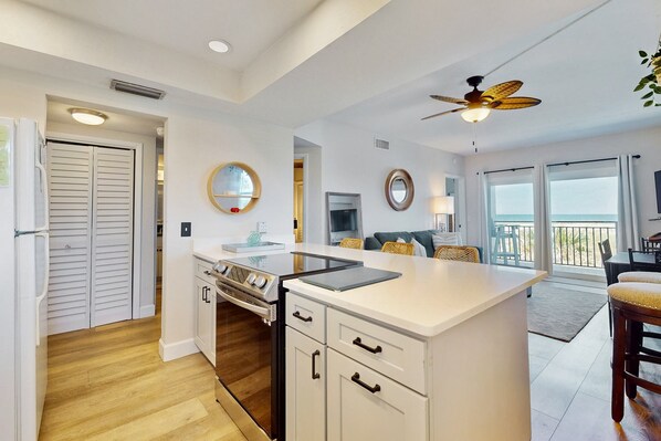 A modern kitchen with white cabinetry, a central island, and a ceiling fan. - Modern Oceanfront Condo With Outdoor Pool, Balcony, & Washer/dryer (Jacksonville Beach)