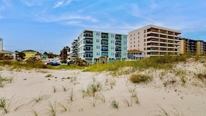 A beachfront hotel with multiple floors, a sandy beach in the foreground, and a clear blue sky. - Modern Oceanfront Condo With Outdoor Pool, Balcony, & Washer/dryer (Jacksonville Beach)