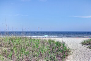 A beach with a sandy path leading to the ocean, some grass in the foreground, and a clear blue sky. - Newly Renovated Oceanfront Condo With Balcony, Wifi, W/D & Shared Pool/tennis (Fernandina Beach)