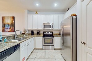 Una cocina moderna con armarios blancos, electrodomésticos de acero inoxidable, encimera de granito y lavavajillas.
