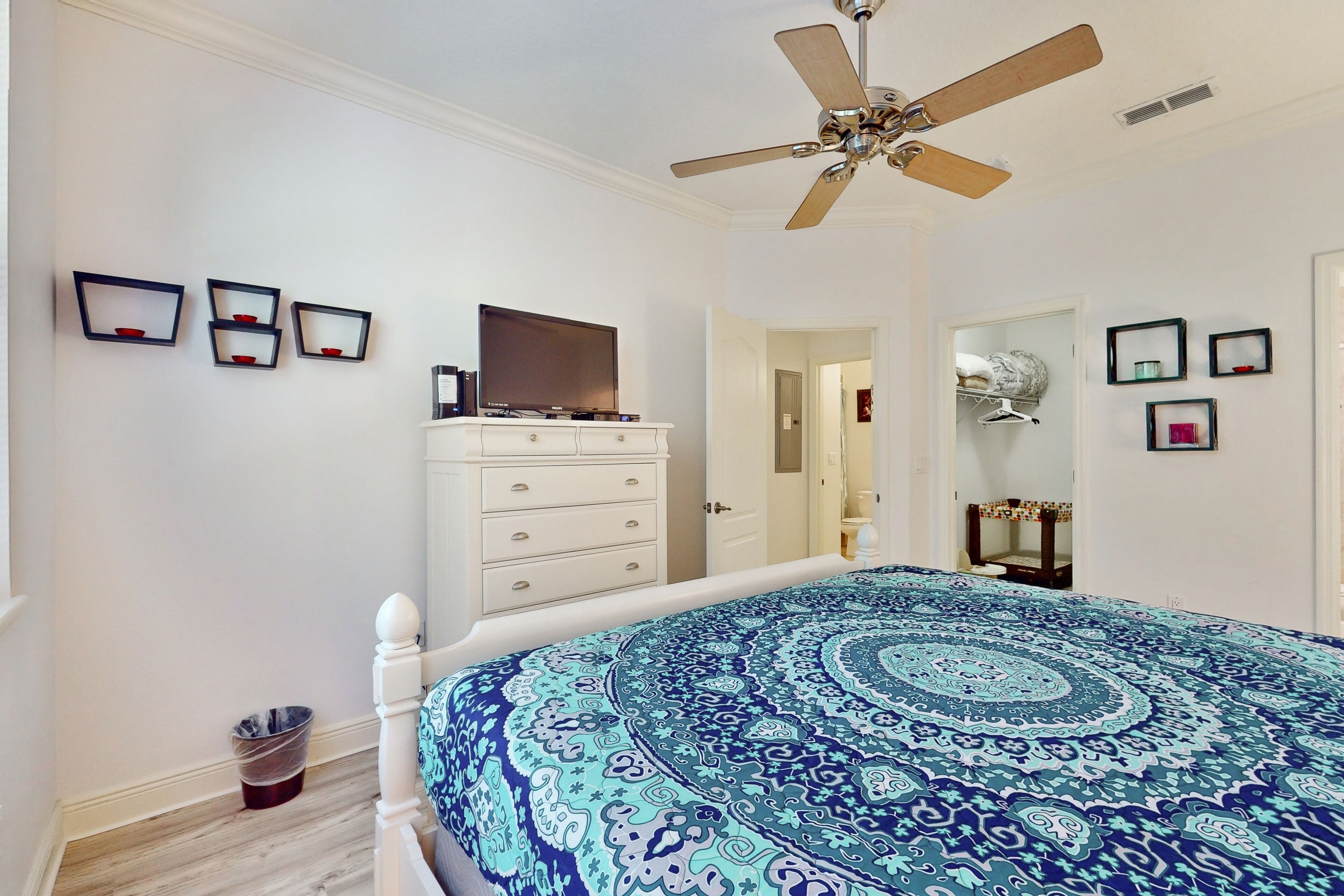 A bedroom with a bed, a ceiling fan, a dresser, and a television.