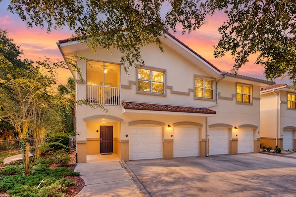 A two-story house with a balcony, multiple garage doors, and a well-maintained garden. - Immaculate Townhome in Upscale Community w/ Pool & Balcony - Near Beach (Palm Coast)
