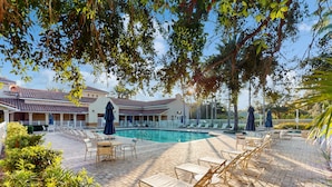 A pool area with lounge chairs and umbrellas, surrounded by a brick patio and greenery. - Immaculate Townhome in Upscale Community w/ Pool & Balcony - Near Beach (Palm Coast)