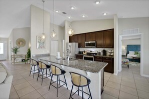 Una cocina moderna con una isla central, taburetes de bar y una zona de comedor con sofá y sillas.