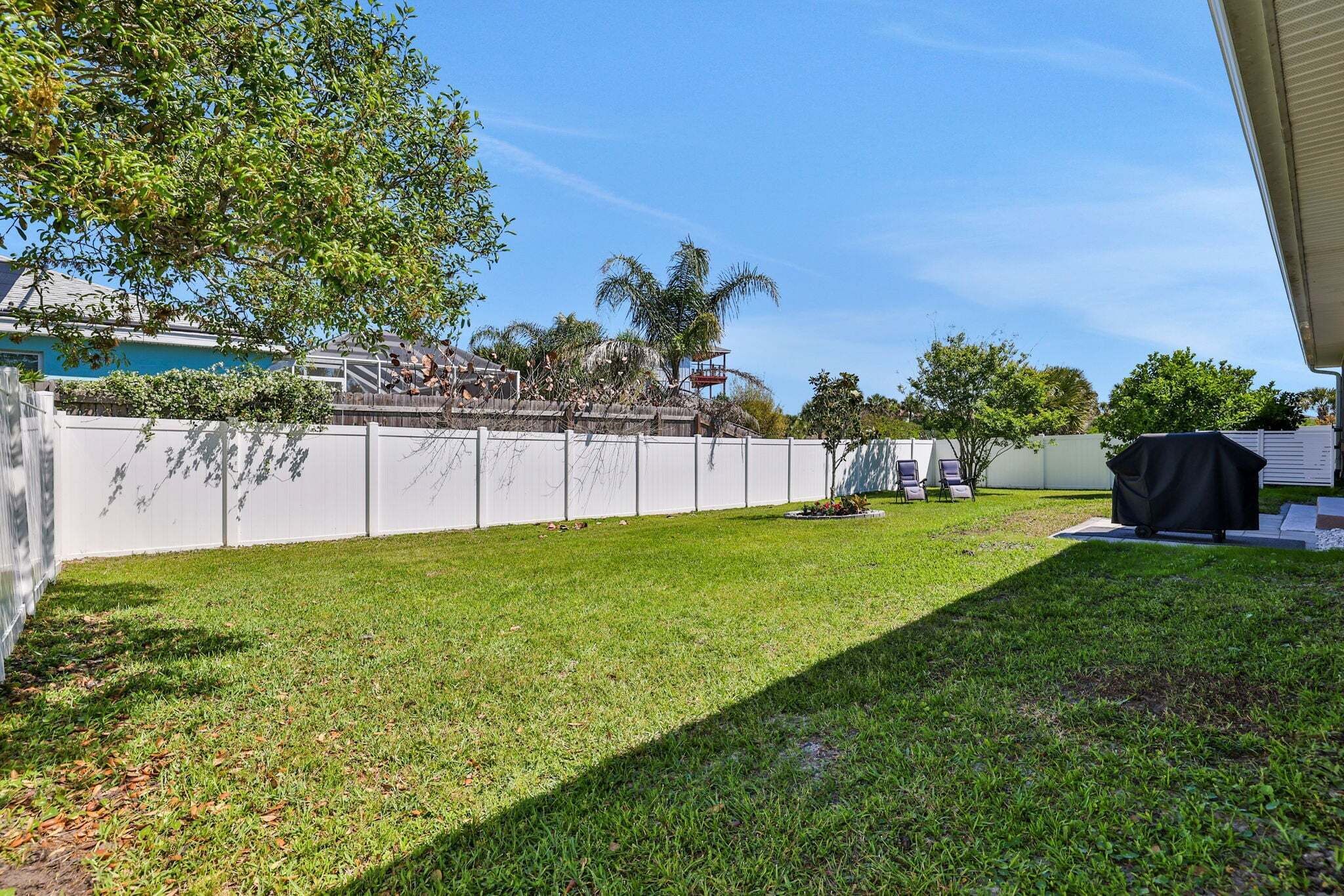 A backyard with a white fence, a pool, and a covered grill area.