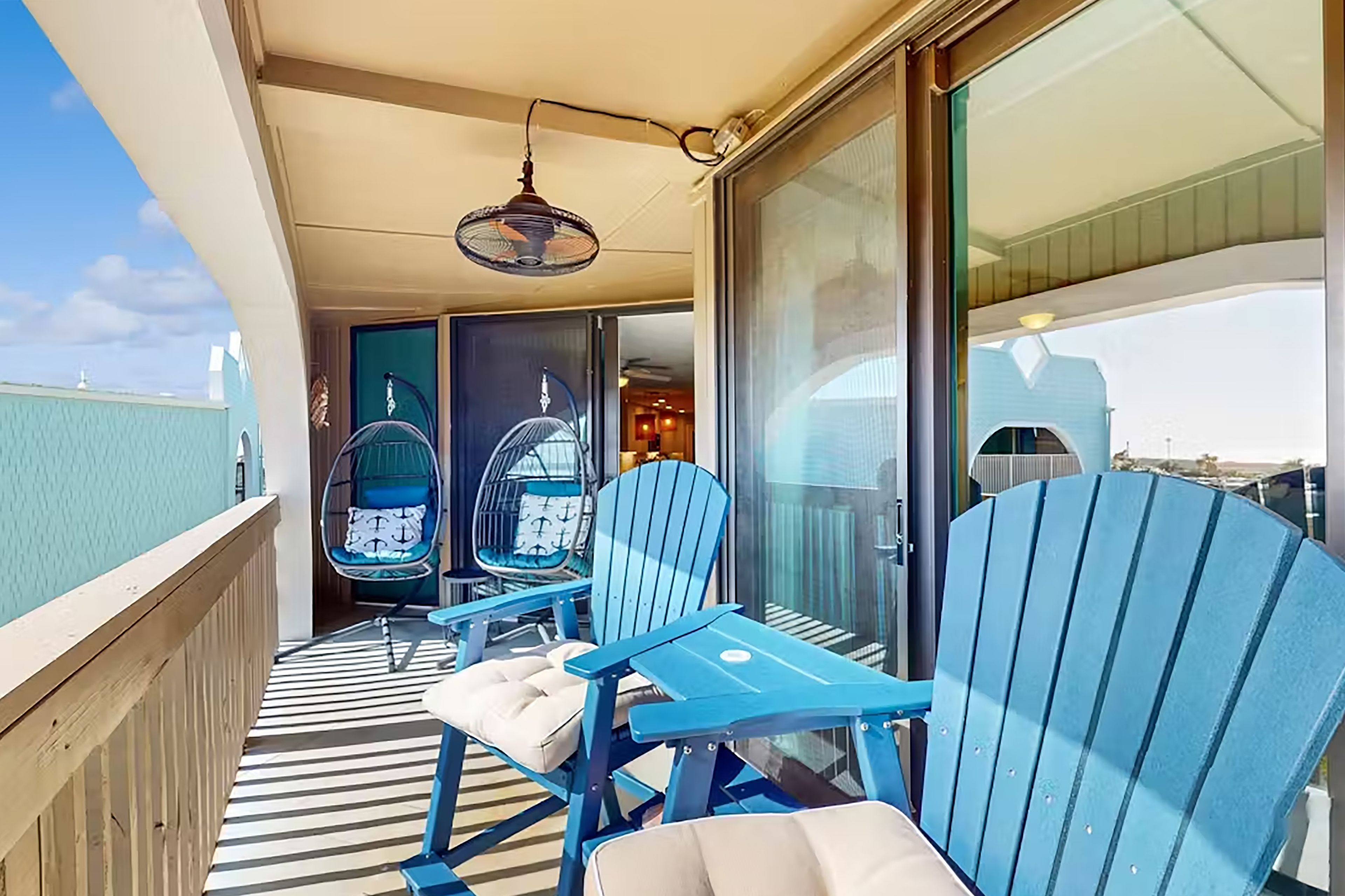 A balcony with blue chairs and a table, a striped floor, and a glass door leading inside.