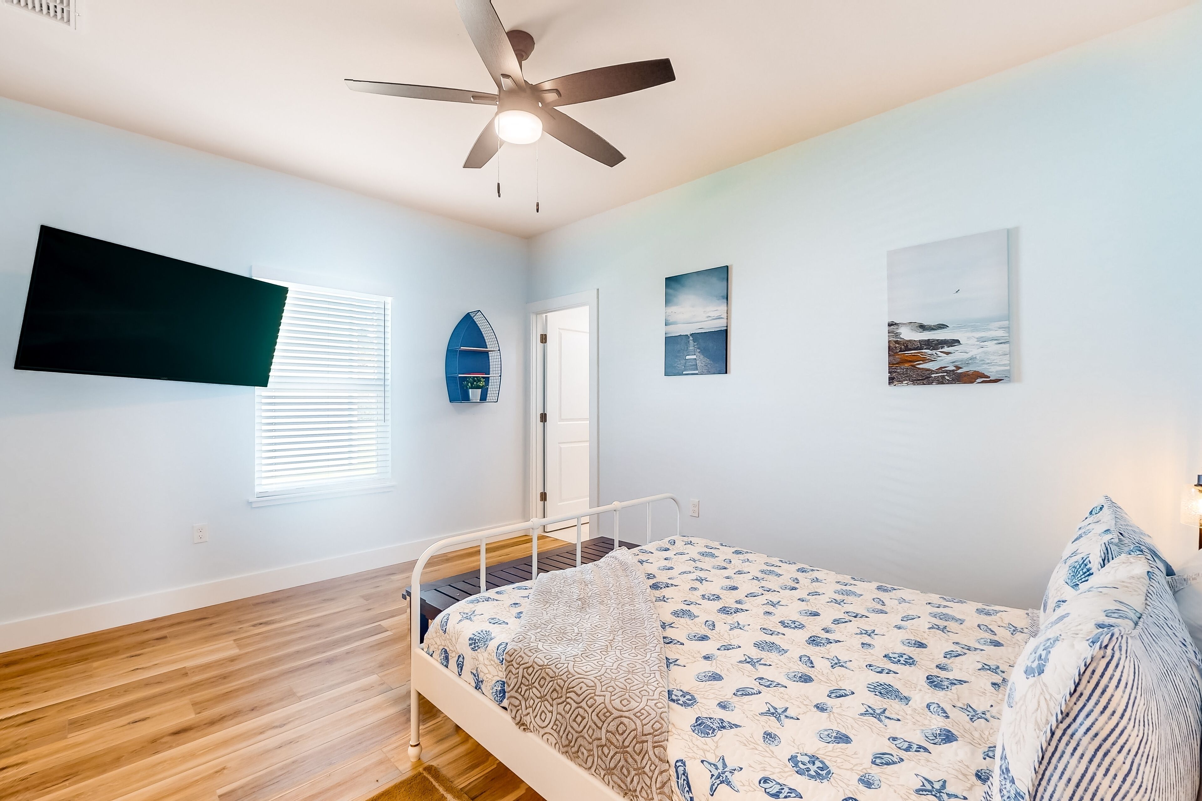 A bedroom with a bed, a ceiling fan, a window with blinds, and a wall-mounted TV.