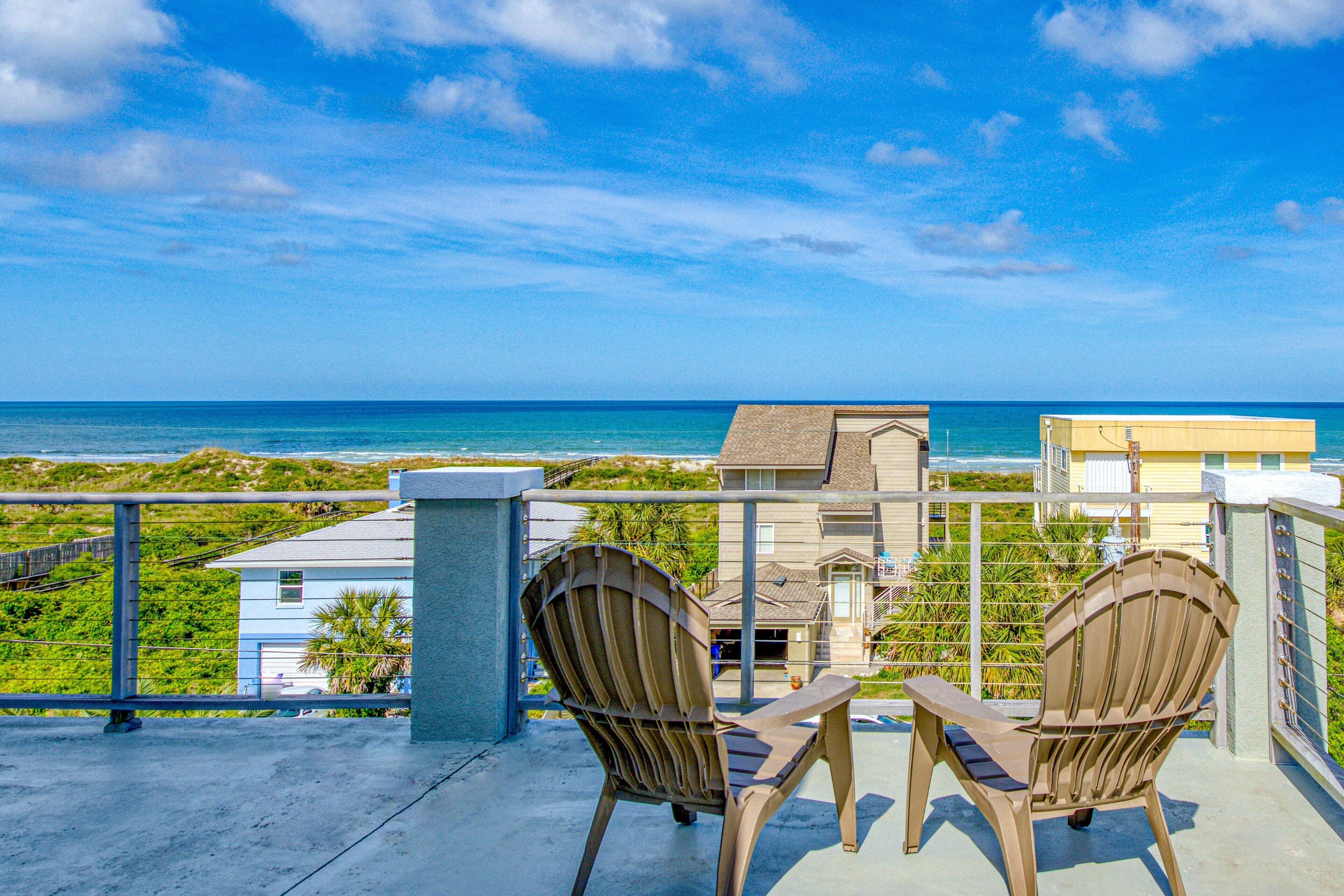 A balcony with two Adirondack chairs overlooking a beach and ocean.