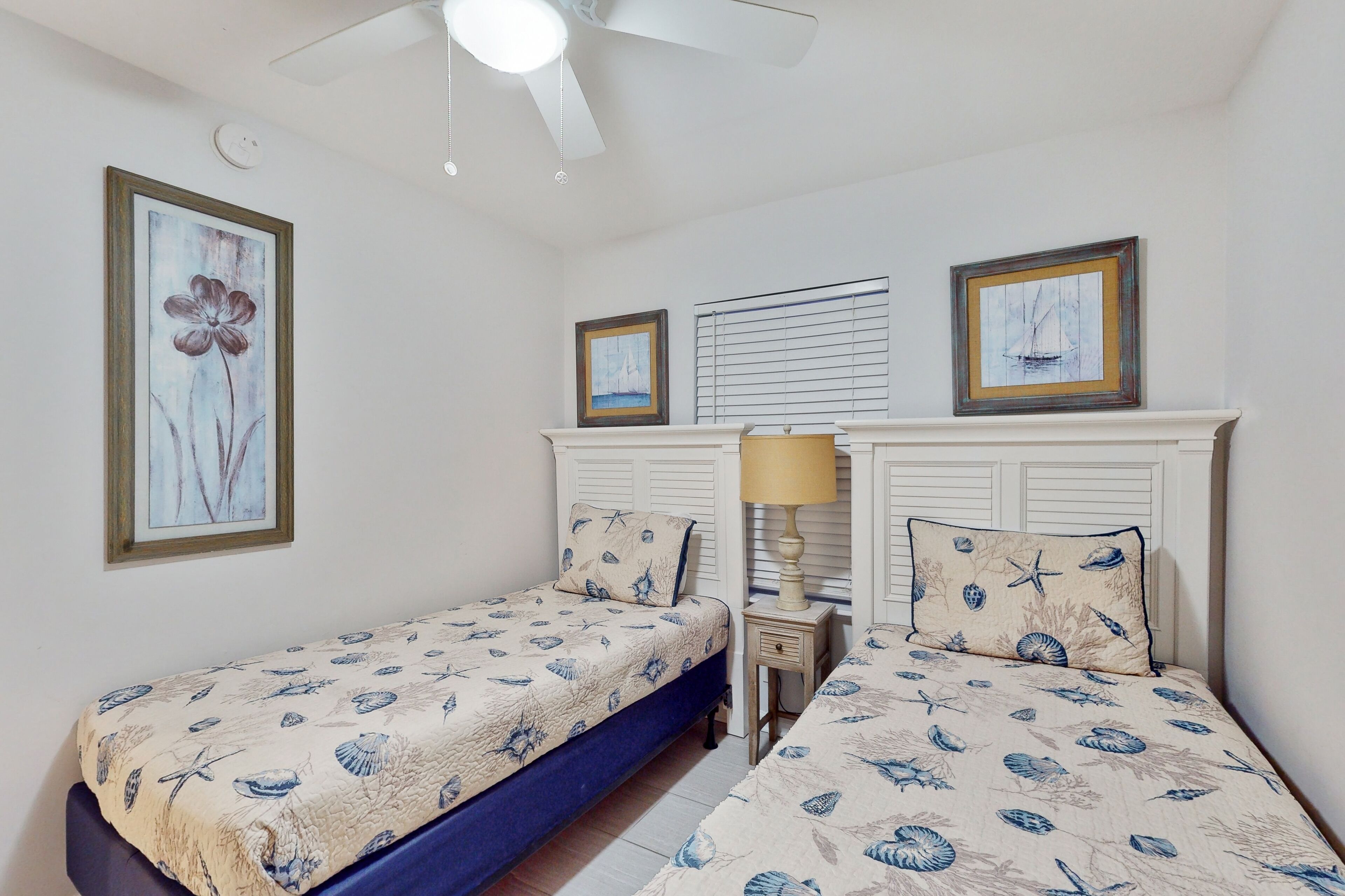 A bedroom with two single beds, a ceiling fan, and framed artwork on the walls.