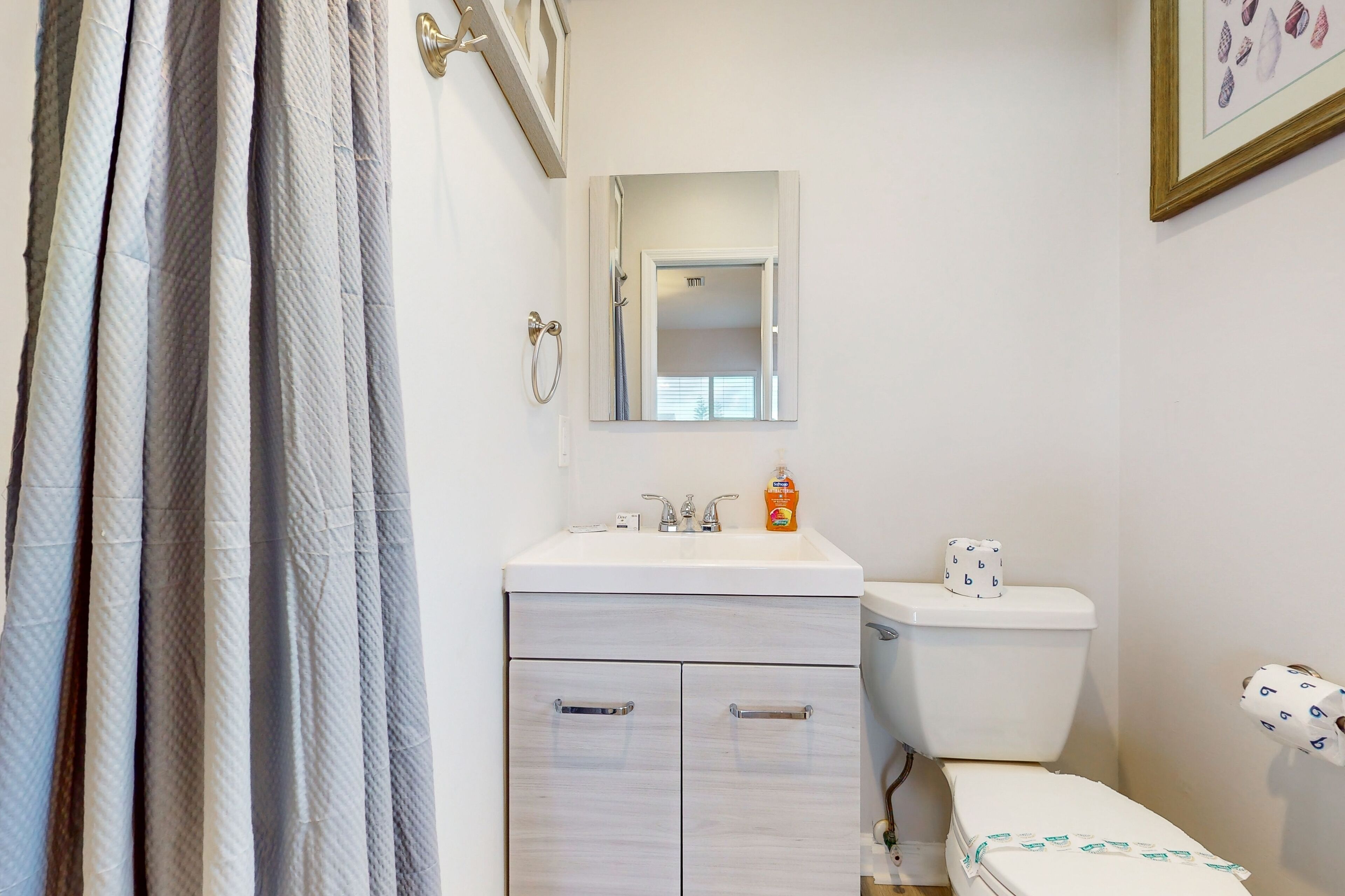 A bathroom with a white sink, mirror, toilet, and a shower curtain.