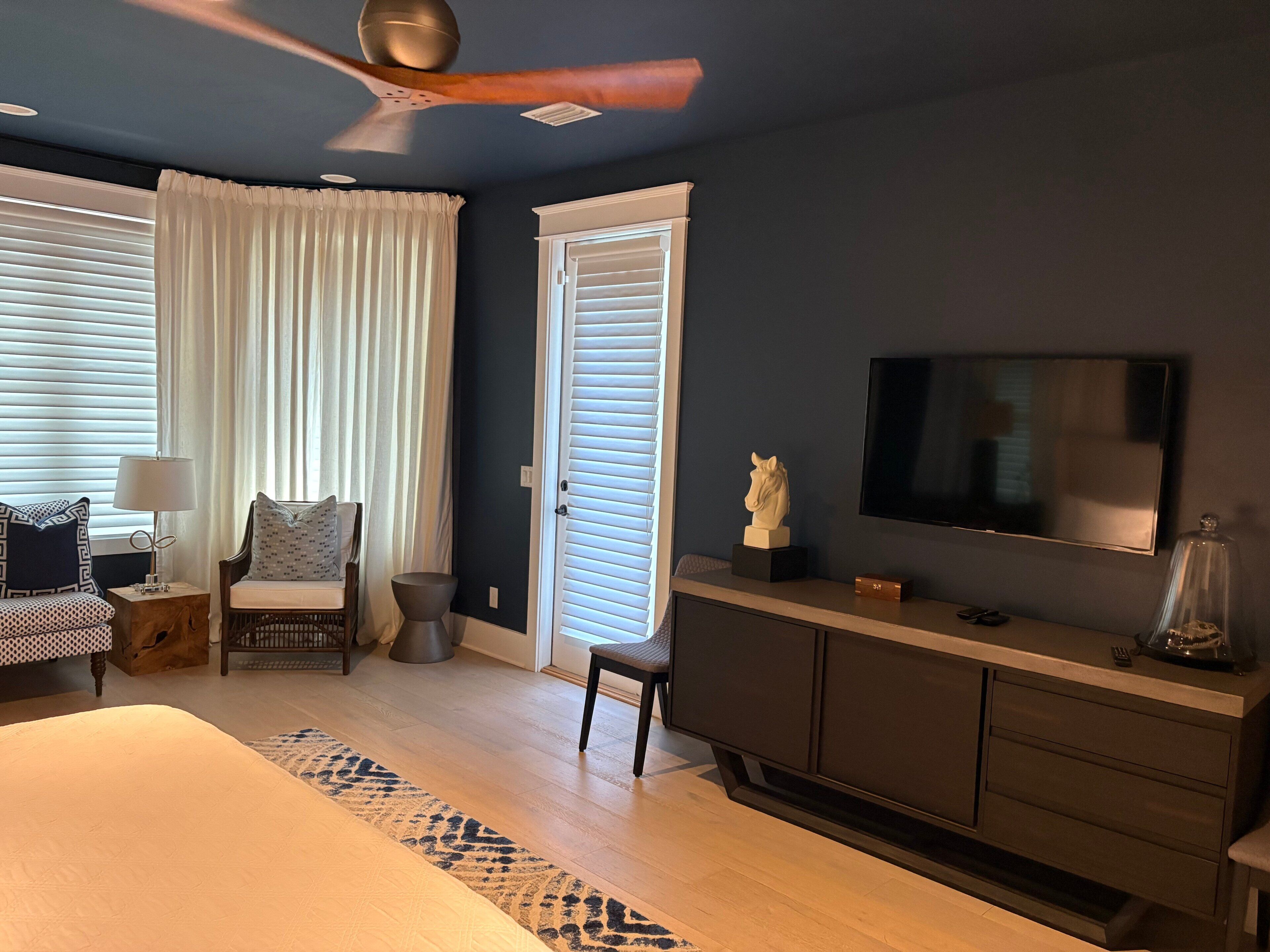 A bedroom with a bed, a desk, a chair, a television, and a ceiling fan.