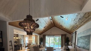 A spacious living area with a high ceiling, a large chandelier, and a view through a sliding door to the outdoors. - Lakefront Home With Private Pool & Outdoor Space for Entertaining (St. Simons Island)