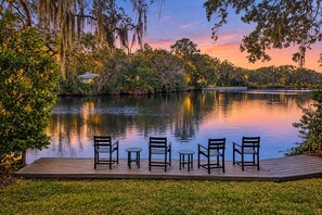 A serene lakeside deck with four chairs and a small table, surrounded by lush greenery and trees. - Lakefront Home With Private Pool & Outdoor Space for Entertaining (St. Simons Island)