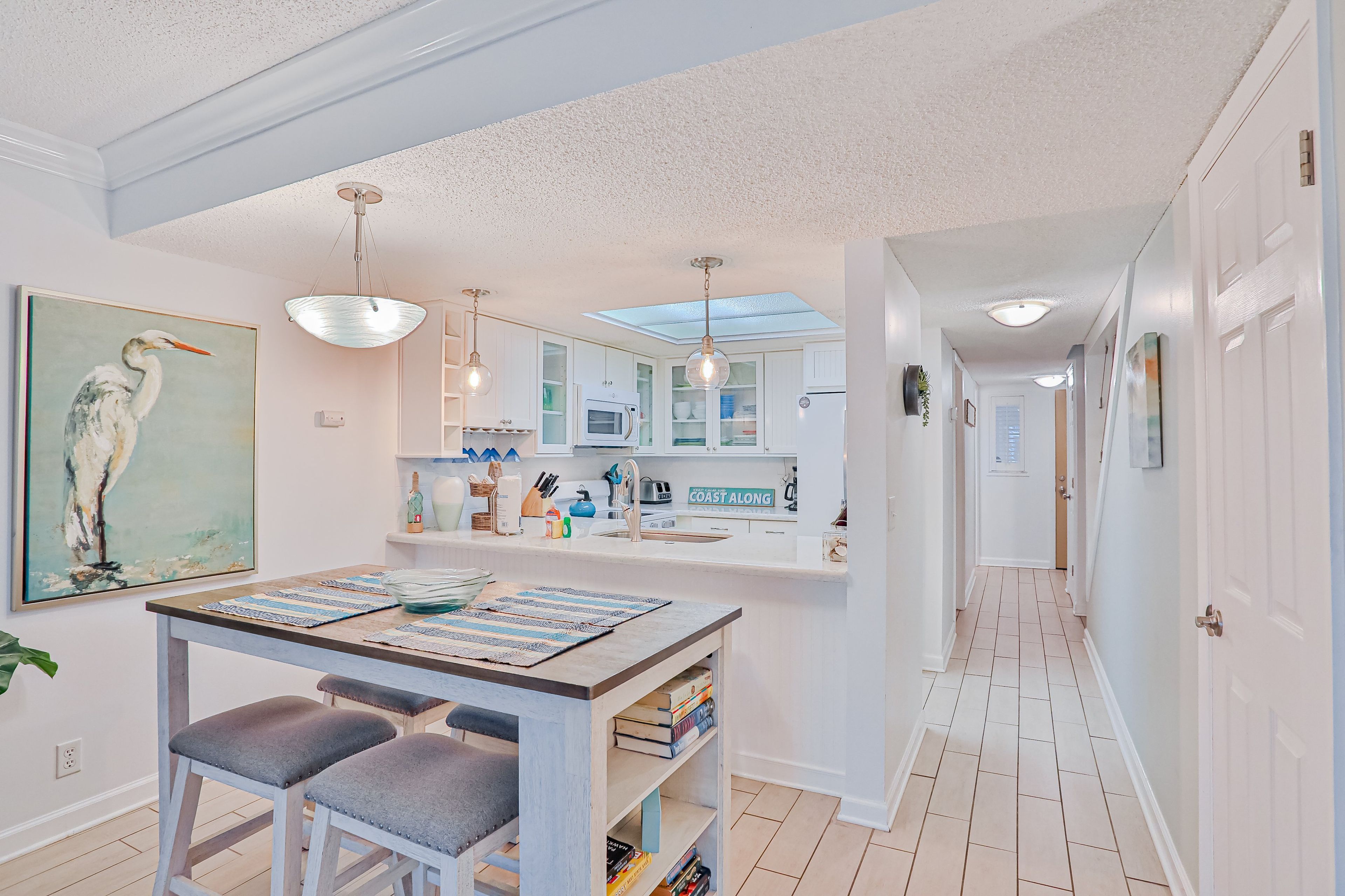 A modern kitchen with white cabinets, a central island, pendant lighting, and a view into the adjacent dining area.