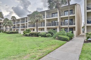 Un edificio residencial de varios pisos con balcones, un césped bien cuidado y palmeras.