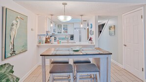 Een moderne keuken met een centraal eiland, barkrukken en een schilderij van een vogel.