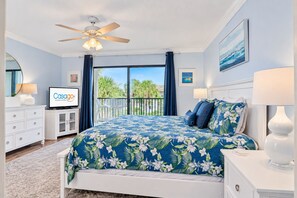Une chambre à coucher comprenant un lit, un ventilateur de plafond, une télévision, un balcon avec des rideaux et une vue sur l’extérieur.